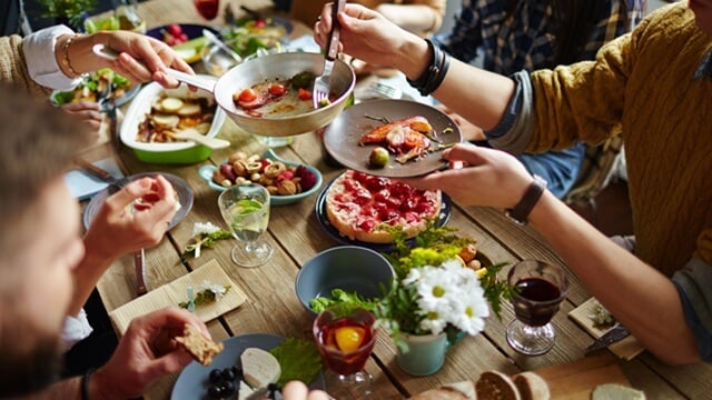 Group of friends sharing a meal at a rustic wooden table with assorted dishes and drinks.